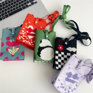 Assorted knit phone bags featuring heart, panda, and floral patterns on a white desk