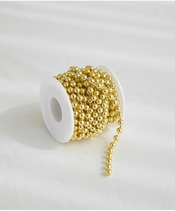 Roll of gold beaded chain on white spool for Christmas tree decoration and DIY crafts
