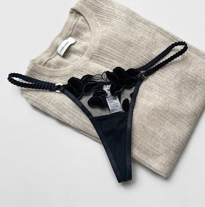Detailed close-up of velvet flower embroidery on sheer mesh thong with gold metal ring