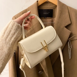 Cream white PU leather crossbody bag with gold buckle and top handle shown on blazer