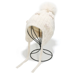 Detail of cream knit trapper hat for girls featuring plush pom-poms and ribbon bows