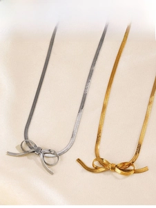 Detail of gold and silver bow-shaped snake bone necklaces on beige satin fabric