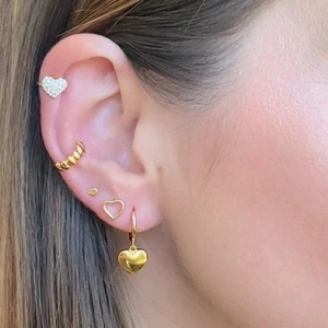Detailed close-up of a golden heart stud and textured ear cuff set on model