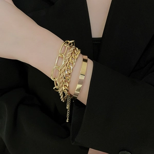 Close-up of layered gold chain bracelet set featuring wide cuff and link designs