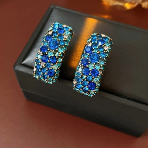Détail de boucles d'oreilles bohèmes dorées serties de cristaux bleus et sarcelle