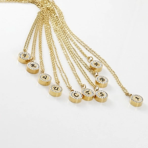 Golden 18K titanium steel necklaces with crystal-rimmed letter pendants on white background