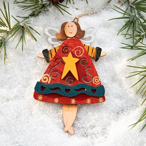 Wooden Christmas angel ornament with red skirt on snow and pine branches for tree decor