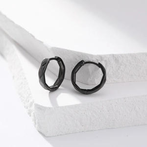 Detail of matte black geometric faceted sterling silver hoop earrings on a stone background