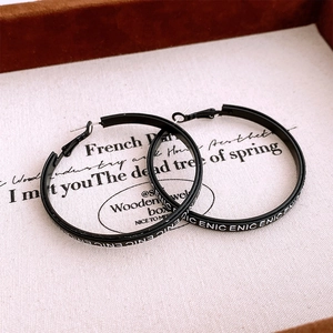 Close-up of matte black round drop earrings with white ENIC lettering on the edge