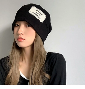 Close-up of a black knitted beanie featuring a white embroidered patch on a model