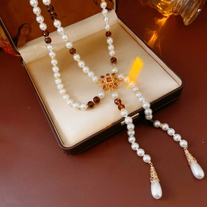Detail of vintage Y-shaped long necklace with white pearls and amber beads in a jewelry box