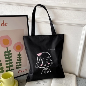 Detail of black canvas tote bag featuring a cute white line art girl and yummy text