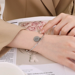 Close-up of a silver stainless steel open bangle with a vintage coin charm on a lifestyle background
