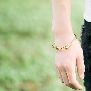 Minimalist gold double-layered open bangle with spherical accents on outdoor background