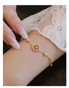 Detailed view of gold starburst compass bracelet with cubic zirconia on model wrist