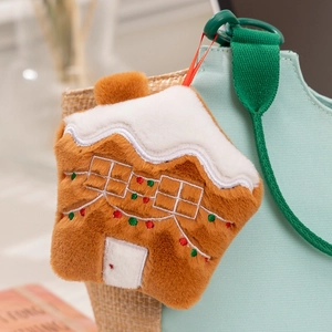 Close-up of plush gingerbread house charm with embroidery hanging on a blue bag
