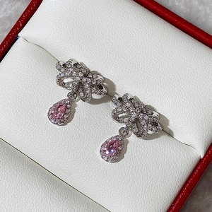 Macro detail of silver bow earrings with pink water drop gems in a red jewelry box