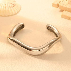 Detail of silver wavy stainless steel bangle on decorative stone and shell background