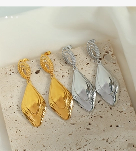 Detailed view of gold and silver geometric leaf-shaped earrings on textured stone