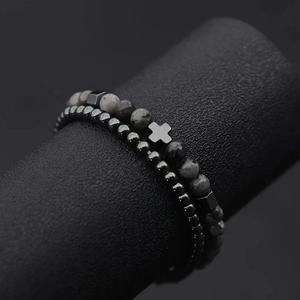 Detail of two beaded bracelets with cross charm on black cylinder display stand