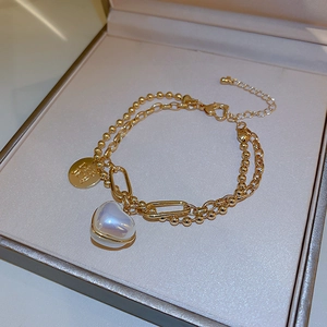 Detail of gold-plated double-layer bracelet featuring a heart-shaped pearl and engraved charm