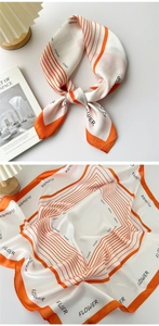 Detail of silk-like square scarf with orange borders and FLOWER print on a minimal desk