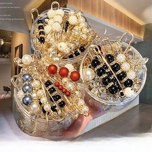 Close-up of assorted faux pearl pins and rhinestone brooches in a transparent jar