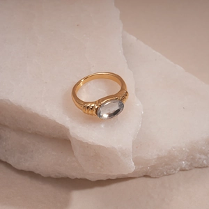 Detailed close-up of golden ring with oval clear gemstone on textured stone base