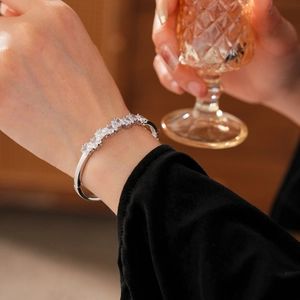 Détail d'un bracelet ouvert argenté orné de huit zircons carrés porté par une main élégante