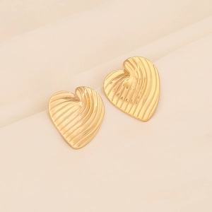 Macro shot of gold heart earrings with unique 3D wavy texture on beige fabric