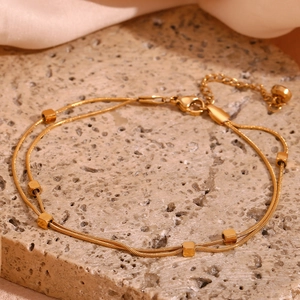 Detail of 18K gold-plated double-layer snake chain anklet with cube beads on stone surface