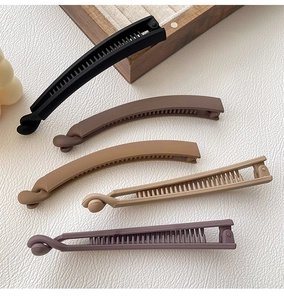 Detail of five matte banana hair clips in neutral colors on a textured surface