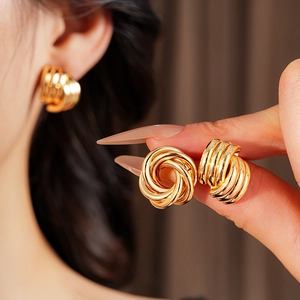 Close-up of golden geometric twisted knot earrings showing refined metallic texture