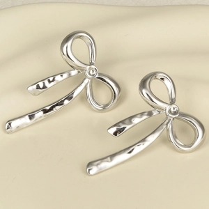 Macro view of silver bow-knot earrings with high-polish finish on cream fabric