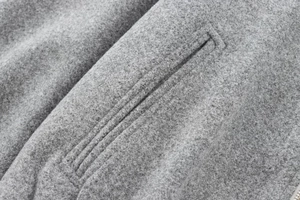 Detailed macro view of gray woolen flight jacket fabric showing stitching and zipper texture