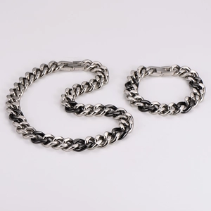 Detail view of silver and black Cuban link chain necklace and bracelet set on white background