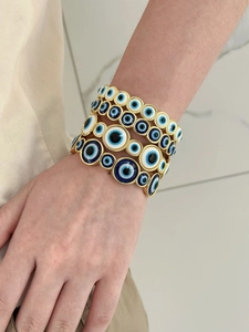 Detail shot of multiple gold-toned bracelets featuring blue evil eye charms on a model's wrist