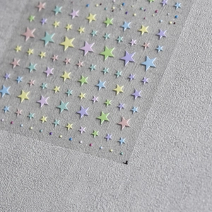 Close-up of embossed star nail stickers in pastel colors and pearl accents on gray surface