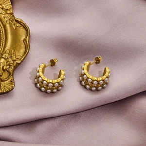 Elegant gold C-shaped earrings with pearls and crystals on purple silk backdrop