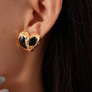 Close-up of golden heart earring with black lava texture enamel worn by model
