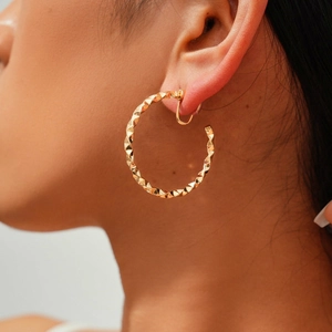 Close-up of model wearing gold geometric textured clip-on hoop earrings without piercing