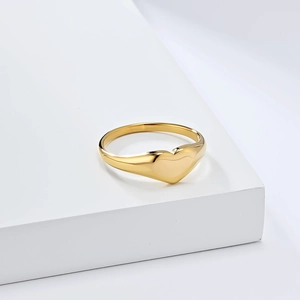 Detailed macro shot of gold polished stainless steel heart signet ring on white pedestal