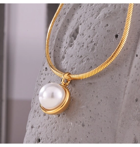 Macro detail of golden snake chain with large pearl pendant on grey stone texture