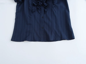 Detailed view of navy blue blouse showing vertical texture, ruffle hem and button closure