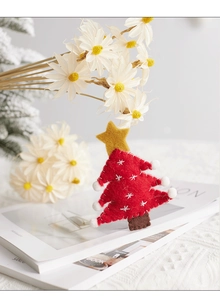 Detail view of red felt Christmas tree ornament with yellow star and white pom-poms on magazines