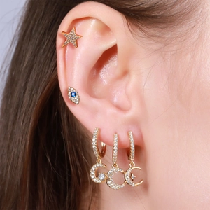 Detail of gold moon pendants and evil eye stud earrings with blue cubic zirconia on ear
