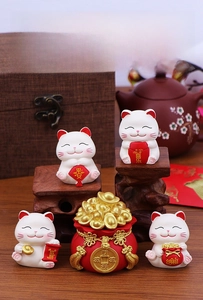 Macro detail of four cute white lucky cats with red treasure bag on wooden base