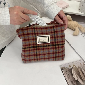 Detail of hand putting cream into a vintage plaid makeup bag with woven texture