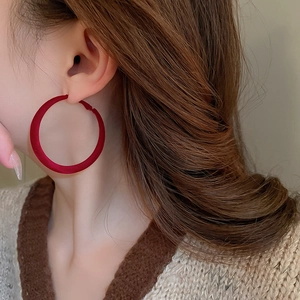 Detail view of large burgundy flocked round hoop earrings worn by a model