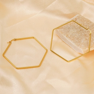 Détail de grandes boucles d'oreilles hexagonales en or 18K sur soie beige avec pierre